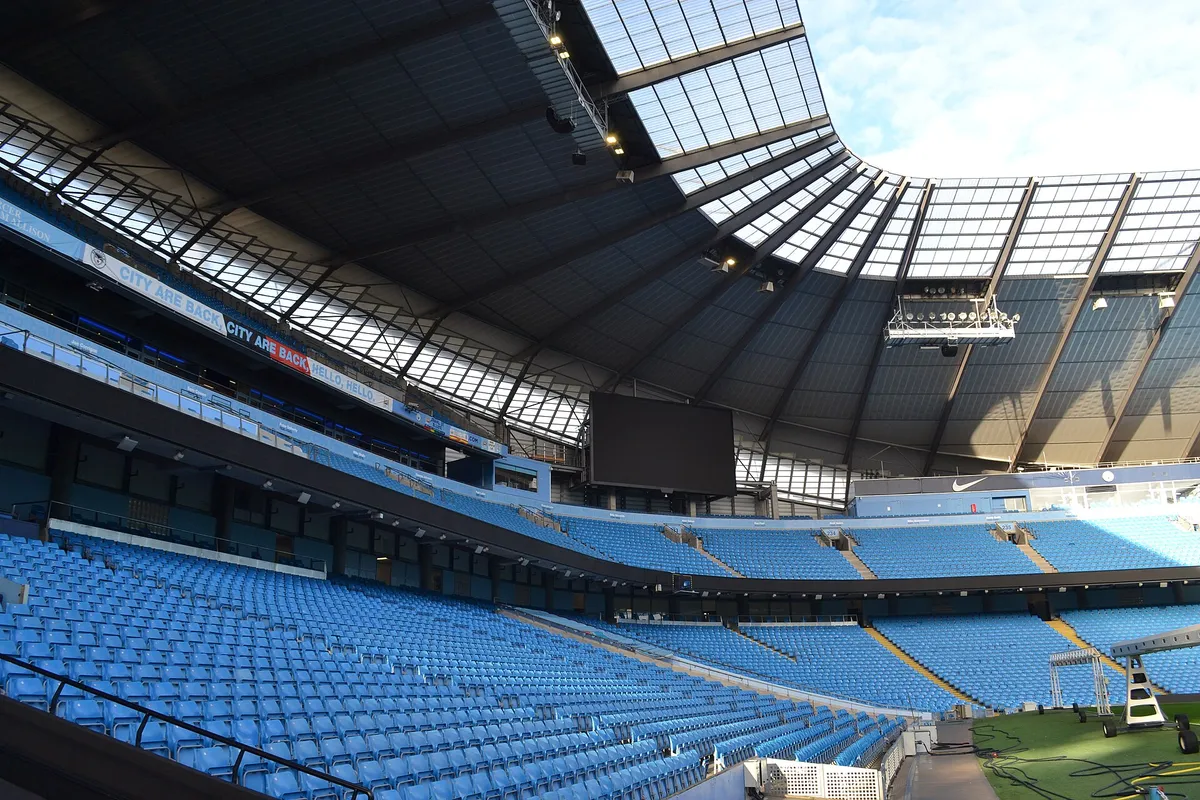 Real stadium-tour view of the Etihad Stadium roof and pale-blue seating