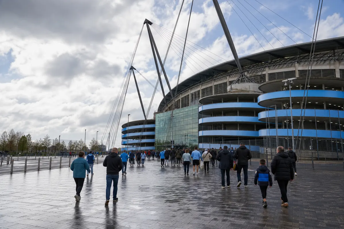 Families and football supporters approaching a large Manchester stadium across the wet exterior plaza